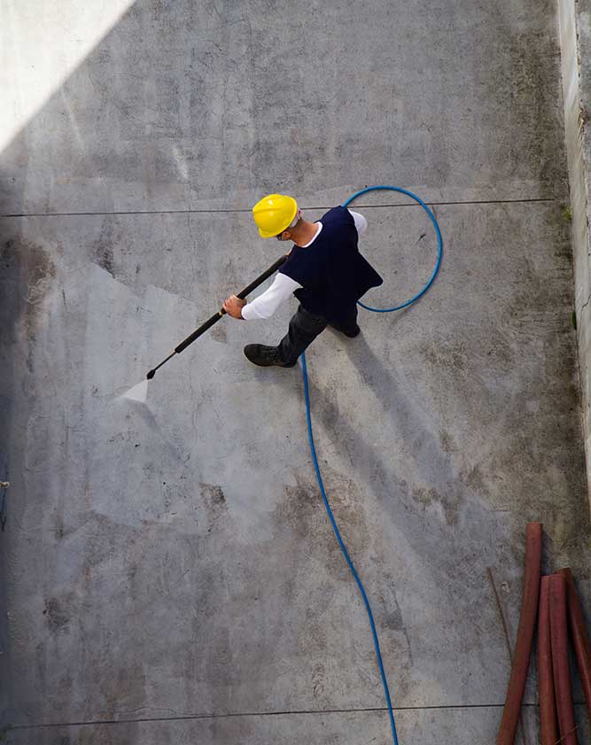 Mann mit gelben Helm von oben, wie er Industrie-Boden reinigt